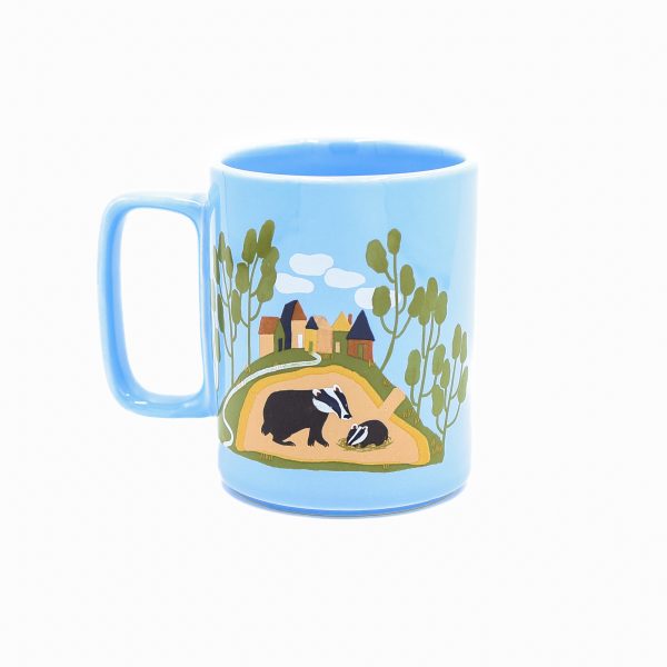 Blue mug with a square handle and paintings of burrow animals on each side. One side is badgers and one side is foxes.