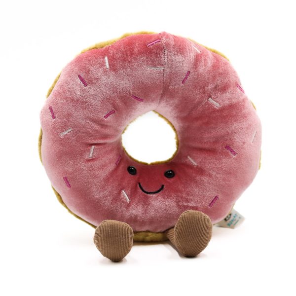 Photographed against a white background, this Jellycat plushie is in the shape of a pink sprinkle doughnut with a smile.