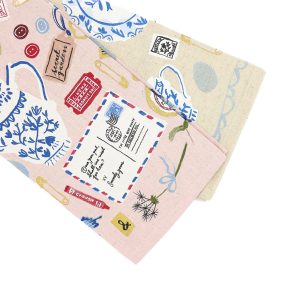 image of a tea towel from above and mostly on the left hand side of the image square. It features a pink background covered with odds and ends such as keys, envelopes, teacups, and other fancy elements.