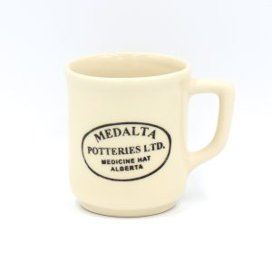 Cream coloured pottery with an angular handle and a black stamp across it spelling the name of the brand: Medalta Potteries Ltd. Medicine Hat Alberta