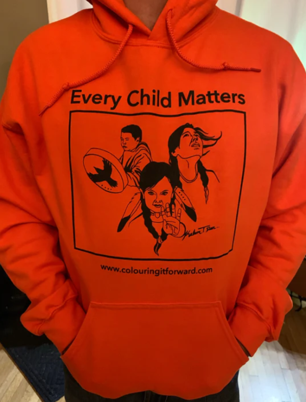 An orange t-shirt with black text on it. The text says "Every Child Matters" and is accompanied by a black graphic of three children in different, relevant poses.