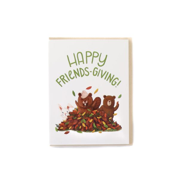 brown card with white envelope, and text that says "Happy Friendsgiving" above an illustration of three animals in a pile of fallen leaves: rabbit, beaver, and baby bear.