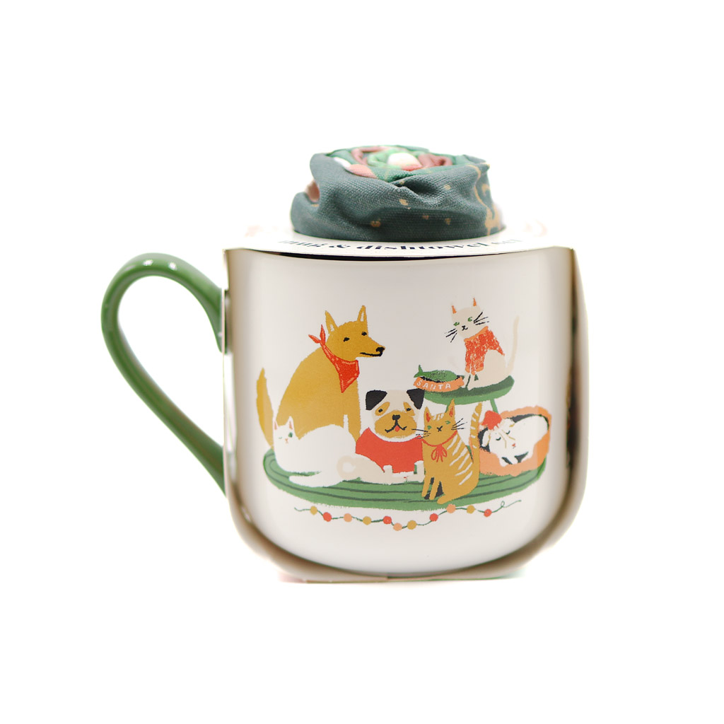white mug with a green handle and a pack of pups waiting for santa on it as the design. The tea towel is similarly patterned, and this time is rolled up inside the mug.