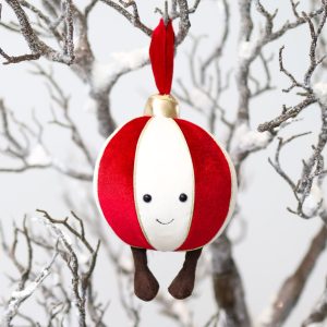 a smiling white, red, and gold ornament hangs from snowwy branches with dangly corduroy legs.