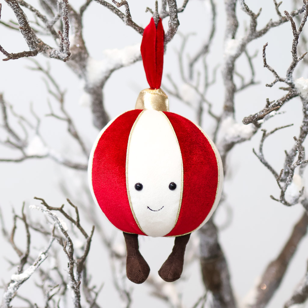 ornament bauble festive christmas jellycat a smiling white, red, and gold ornament hangs from snowwy branches with dangly corduroy legs.