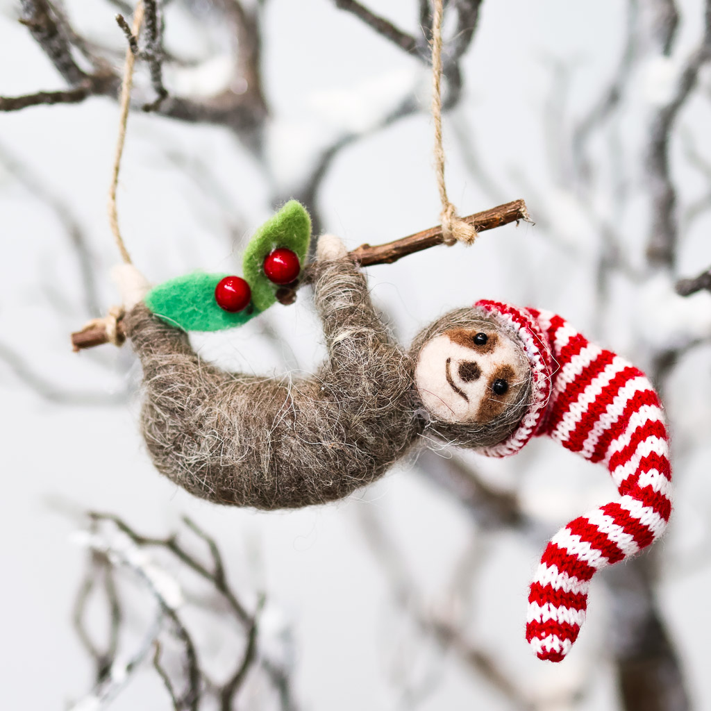 mistletoe sloth ornament a sloth with a smile and a red striped hat is hanging from a branch of mistletoe